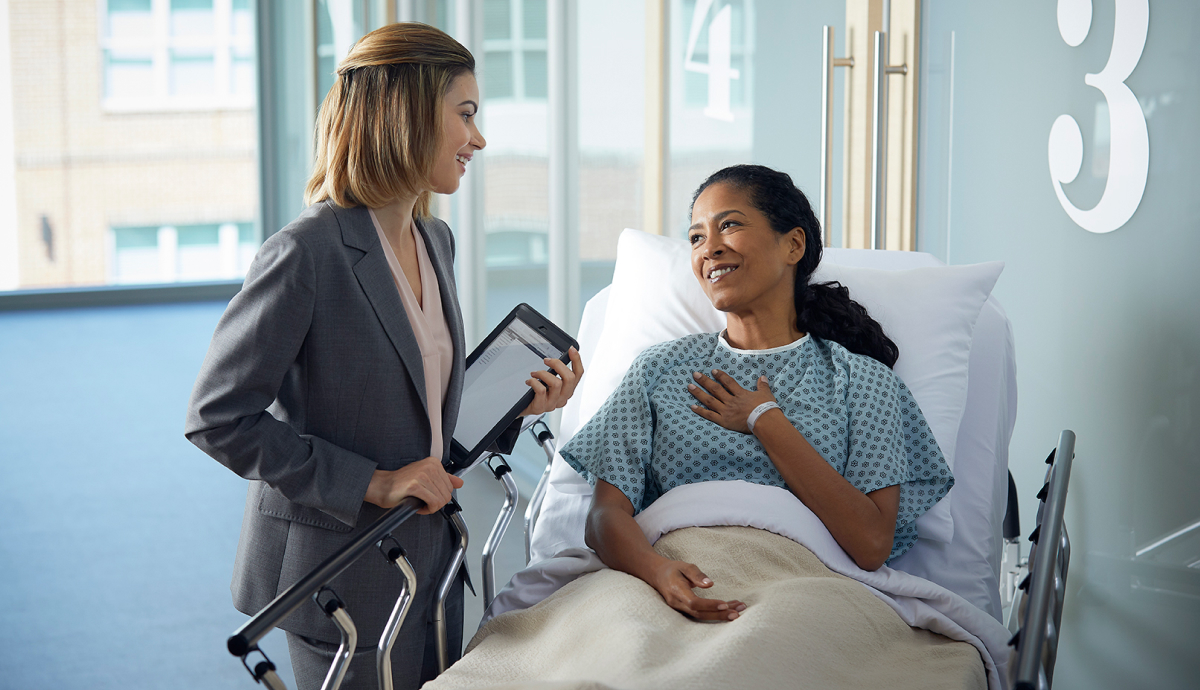 Businesswoman showing tablet to smiling patient in hospital bed, healthcare support service