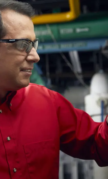 Smiling technician in red uniform and safety glasses working on equipment in industrial facility