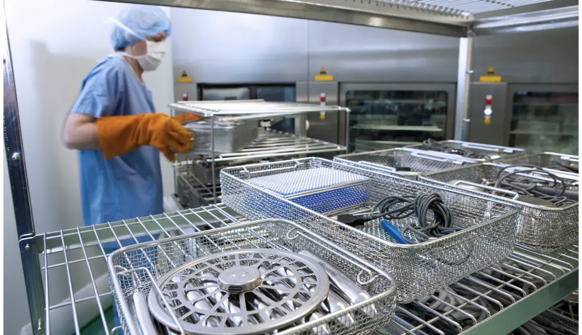 Worker inspecting surgical instruments in sterile metal baskets at healthcare facility