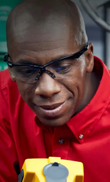 Technician in red shirt and safety glasses examining medical equipment, providing healthcare support services.