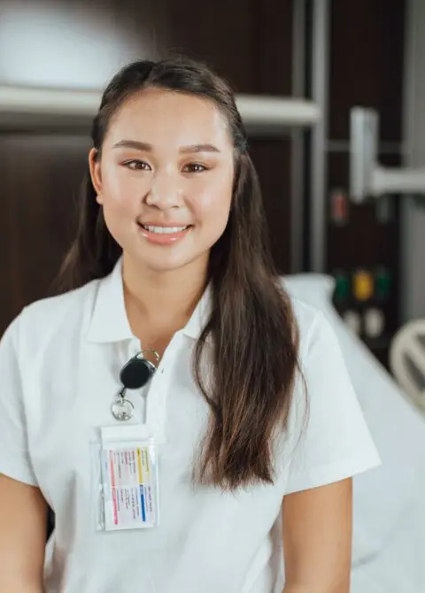 Smiling young female healthcare worker wearing ID badge, white uniform in hospital hallway