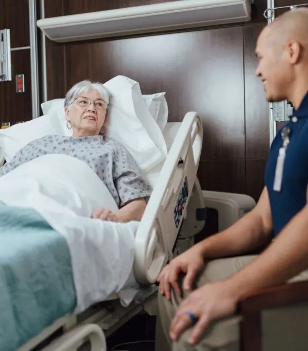 Elderly patient in a hospital bed talking with a healthcare worker