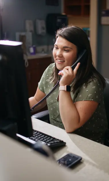 Smiling woman on phone at office desk with computer and calculator