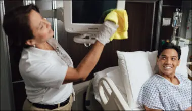 Nurses cleaning hospital room together, smiling at camera in positive healthcare environment.