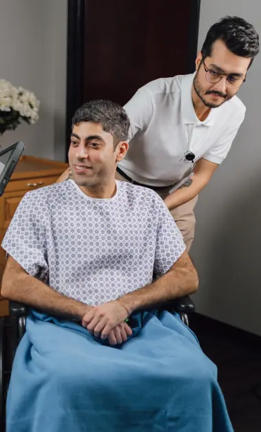 Caring male nurse discussing patient care with seated male patient in hospital gown
