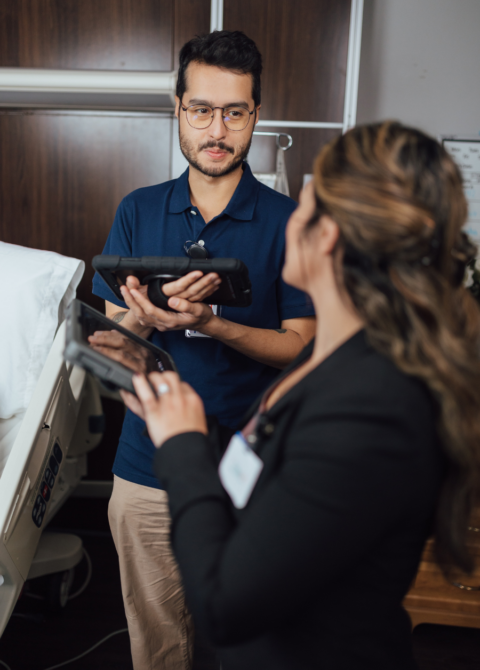 Man wearing glasses holds electronic tablet while talking to woman in office