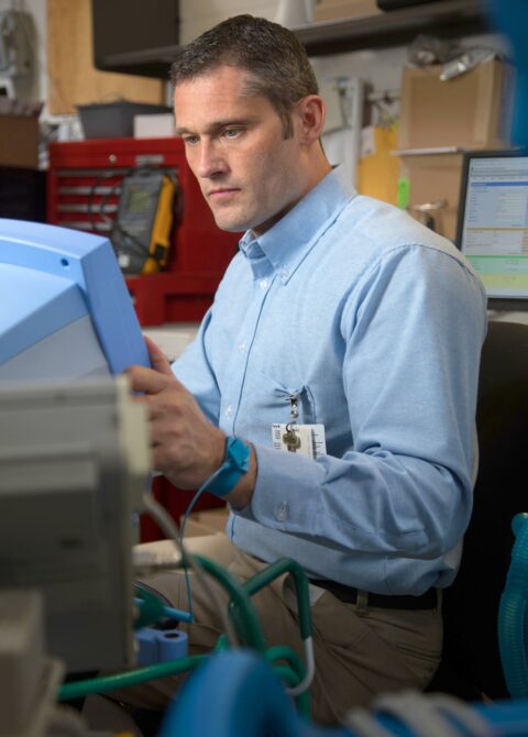 Alt text: Man in blue shirt examines equipment in workshop, focused on task at hand