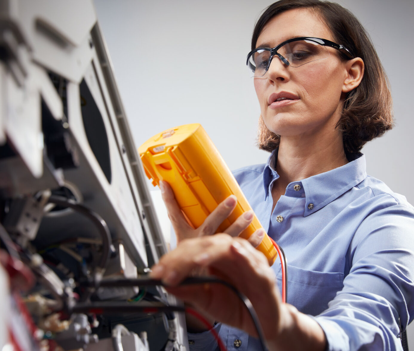 Alt text: Woman in lab coat and safety glasses inspecting medical equipment at healthcare facility